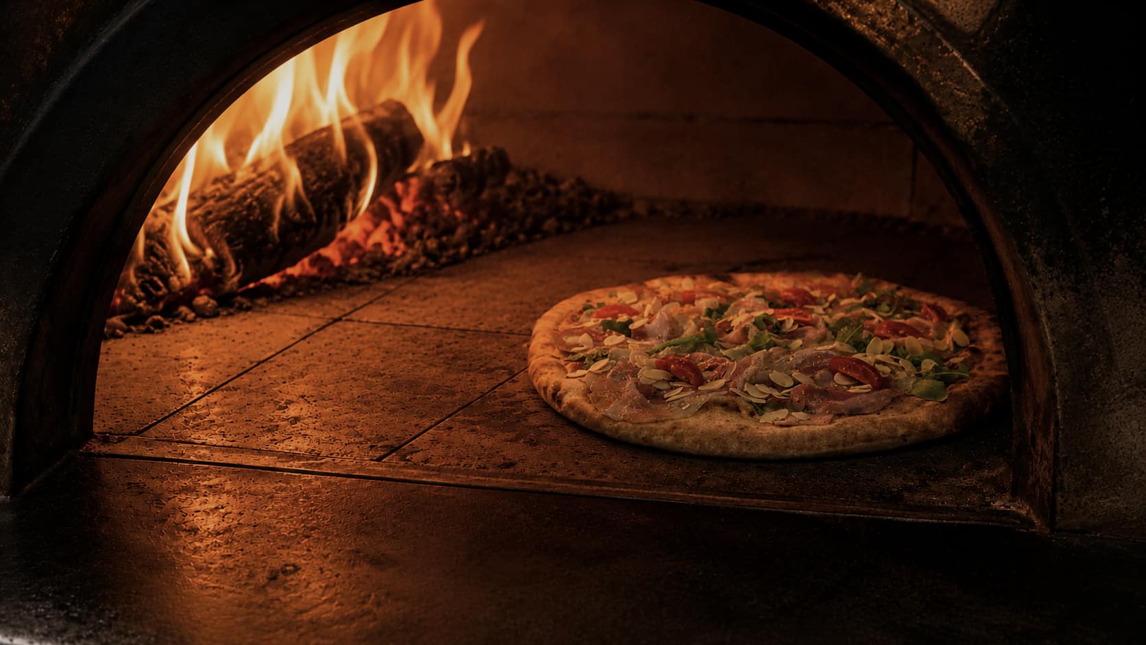 Le four à bois de la Pizzeria Bambino, flammes vives, une pizza en cuisson sur la sole.