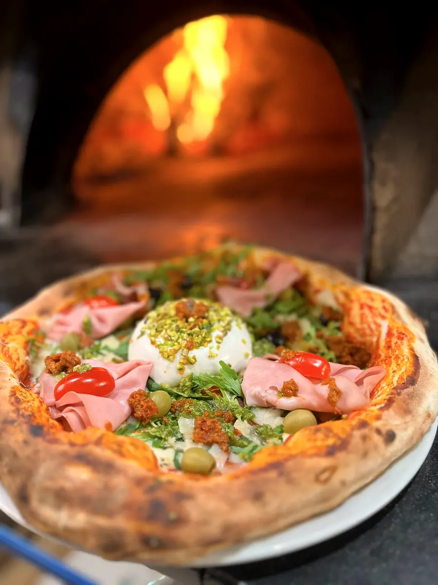 La pizza Estate, burrata, mortadelle et pistache, posée devant la bouche du four.