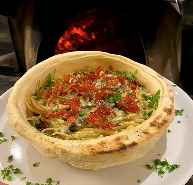Pâtes crémeuses servies dans un pain cuit au feu de bois, garnies de speck croustillant.